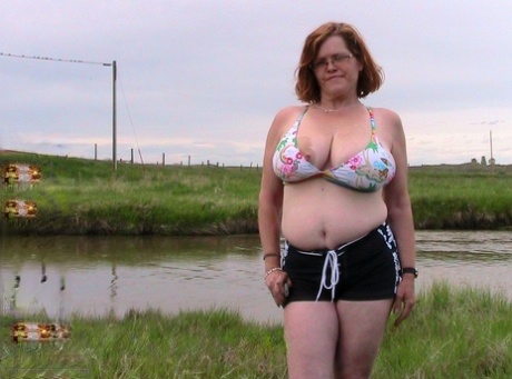 Chubby redhead Misha MILF strips naked in a field near a body of water 80519769